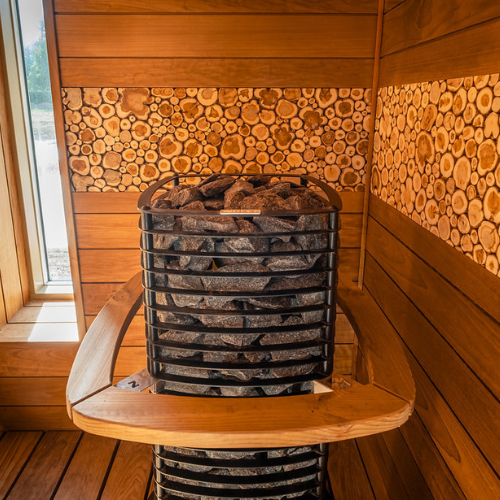 Wooden sauna with a stone stove and stacked logs on the wall.