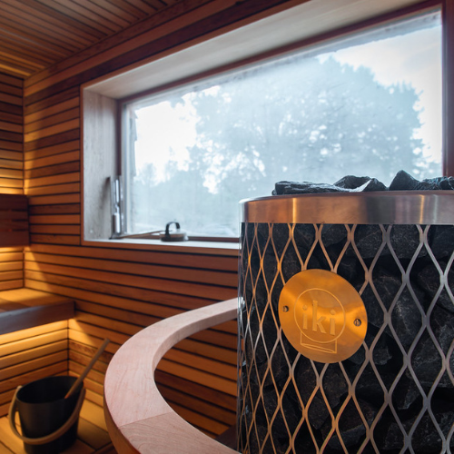 Sauna interior with wooden walls, a large window, and a metal sauna heater with a visible brand logo.