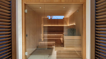 This Bespoke Alder Sauna Installation has a full glass wall, through which you can see a vertically clad sauna using alder tongue and groove cladding, an L shaped sauna bench system with an upper and lower bench and a Narvi Velvet Electric Sauna Heater.