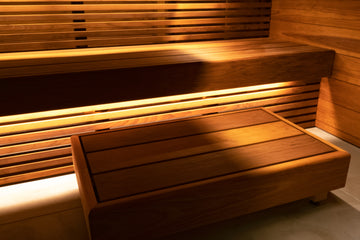 Thermo Aspen Bespoke Sauna Installation. The photo depicts a thermo aspen upper and lower bench sauna, with under bench skirting that is lit by concealed sauna strip lighting. There is a moveable sauna step also made from Thermo Aspen.