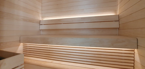 Aspen Wood Bespoke Sauna Installation. The bespoke aspen sauna installation has an upper and lower bench, backrest, hidden sauna strip lighting, under bench skirting and a heater guard.