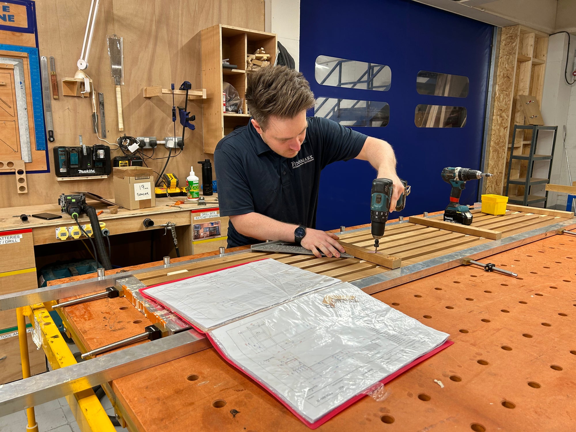 Person using a drill in a workshop setting with tools and materials around