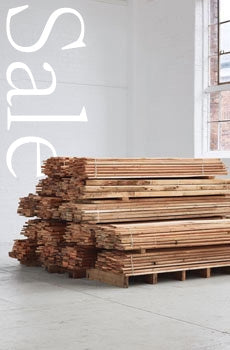 Stack of wooden planks with 'Sale' sign on a white wall