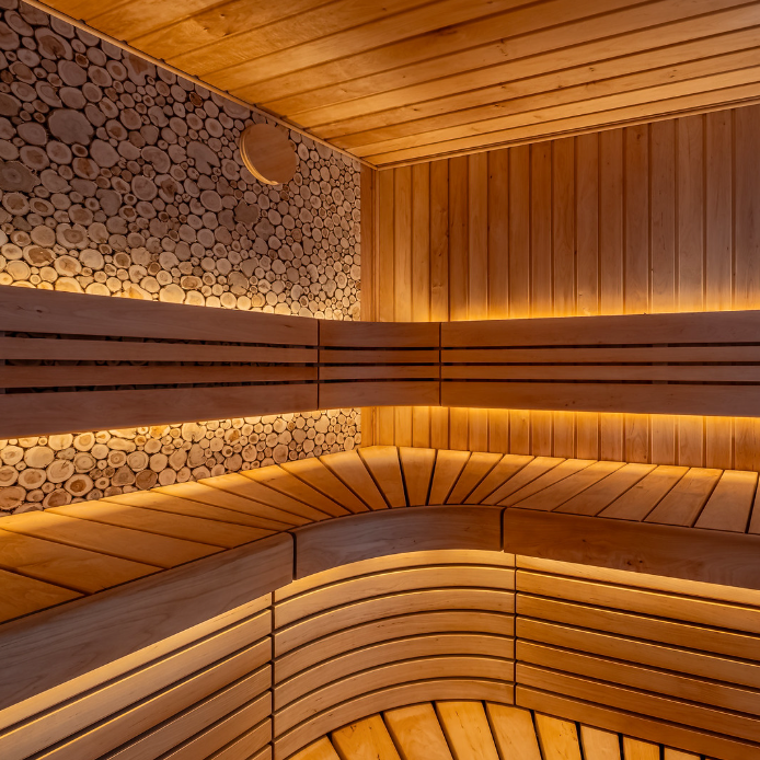 Wooden sauna interior with curved bench and stacked logs on the wall.