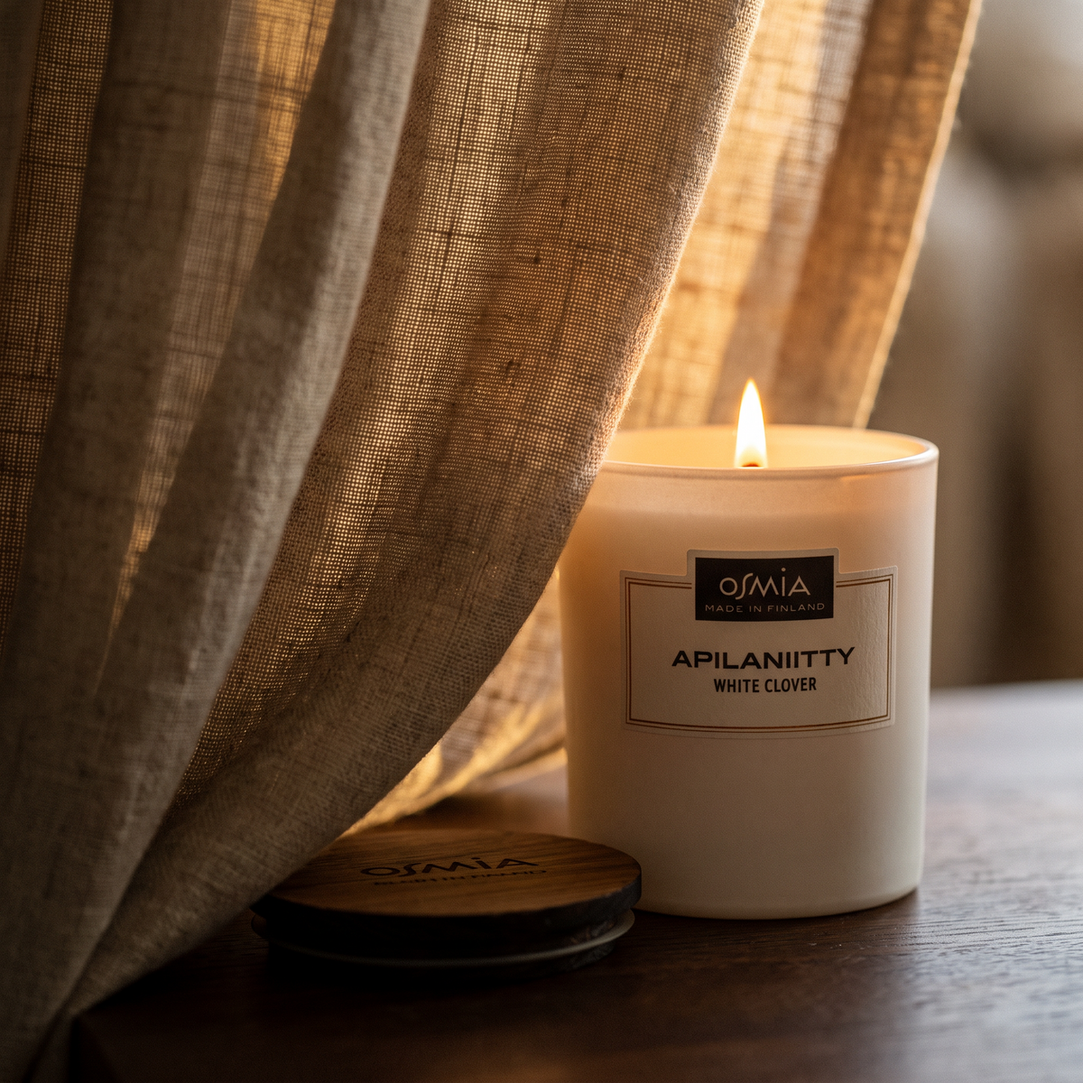 White Clover Scented Candle by Osmia - lit behind linen curtain