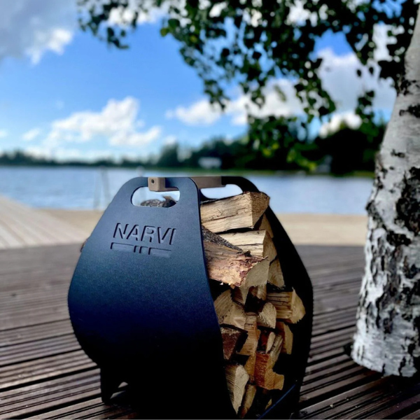 Black metal firewood holder with stacked firewood on a wooden deck by a lake.